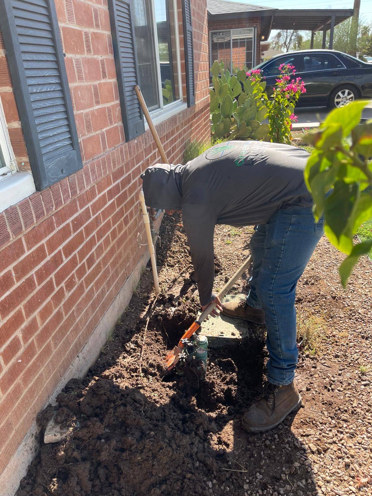 Crew member uncovering irrigation valves next to a brick house